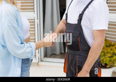 Handschlag zwischen einer Hausangestellten im Overall und einer Kundin. Repräsentiert eine erfolgreiche Vereinbarung. Vertrauen. Geschäftspartnerschaft. Und relia Stockfoto