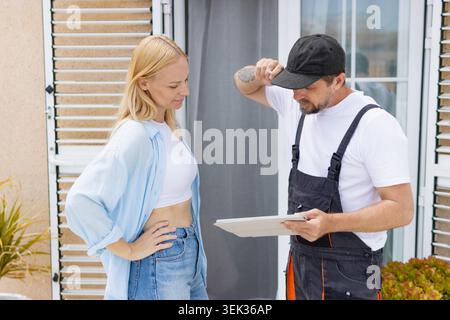 Hauseigentümer sprechen mit einem professionellen Techniker in Uniform und prüfen Serviceverträge und Reparaturpläne auf einem digitalen Tablet beim Kunden Stockfoto
