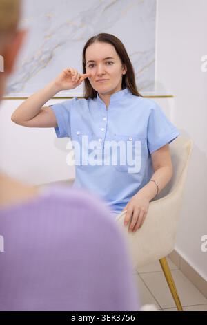 Junge Frau in einer hellblauen Uniform, die Gebärdensprache unterrichtet, Gesten zu einem unsichtbaren Schüler und fördert Kommunikation und Inklusivität in der Bildung für die Stockfoto