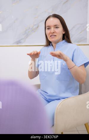 Frau in hellblauer Uniform führt ein animiertes Gespräch mit Handgesten, um einen Patienten während einer medizinischen Konsultation zu erklären oder zu beraten Stockfoto