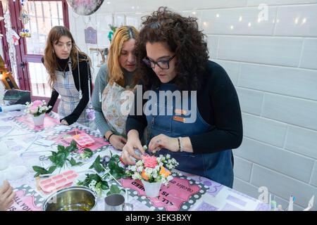 Frauen, die an einem Workshop teilnehmen und hausgemachte Kerzen mit Blumen und kreativen Elementen dekorieren Stockfoto