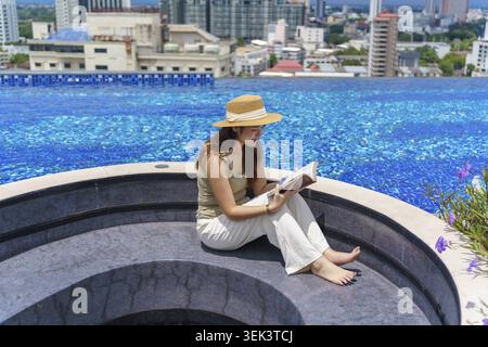 Sommerurlaub Junge asiatische Frau schöne Frau, die Buch liest und sich im Swimmingpool entspannt Stockfoto