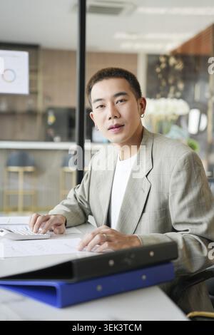 Lächelnder junger asiatischer Geschäftsmann im modernen Büro. Gutaussehender asiatischer Mann, glücklich und freundlich bei der Arbeit, Erfolg, Job Stockfoto