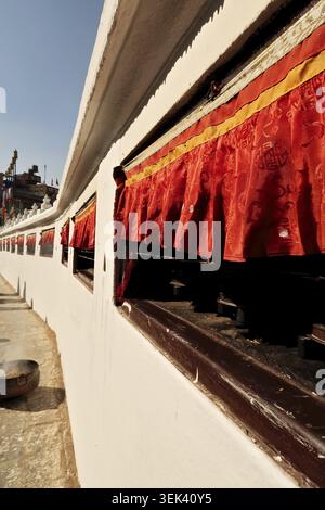 Lange Reihen von Gebetsrädern mit roten Vorhängen sind in die Außenwände der Boudhanath Stupa in Kathmandu (Nepal 2022) eingebaut Stockfoto