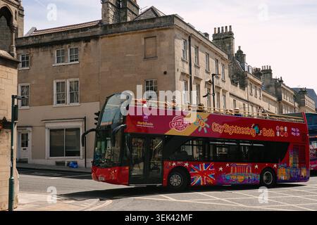 Roter Doppeldeckerbus mit offenem Oberdeck, der auf der Straße vorbei an historischen georgianischen Kalksteinbauten in Bath, Somerset, England fährt Stockfoto