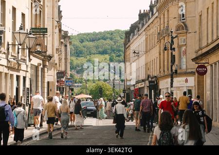 Die geschäftige Westgate Street in Bath, Somerset, Großbritannien, ist voller Menschen, die unter klarem Himmel an Geschäften und historischen Kalksteinbauten vorbeilaufen Stockfoto
