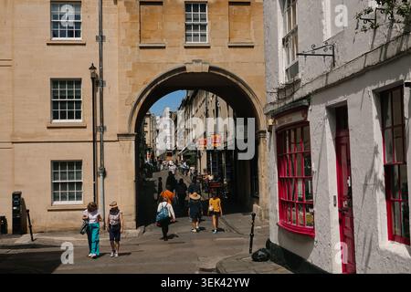 Fußgänger, die durch den historischen Steinbogen der Trim Bridge auf einer schmalen Straße im Stadtzentrum von Bath, Somerset, Großbritannien, spazieren Stockfoto