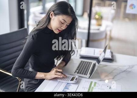 Schöne selbstbewusste asiatische Geschäftsfrau, die mit Laptop und Tastatur arbeitet. Professioneller Investor arbeitet an einem neuen Start-up-Projekt. Unternehmen Stockfoto