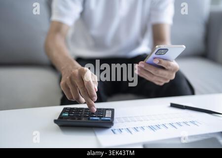 Der Mann berechnet die Finanzen zu Hause, bezahlt Rechnungen, Steuern am Handy und Rechner Stockfoto