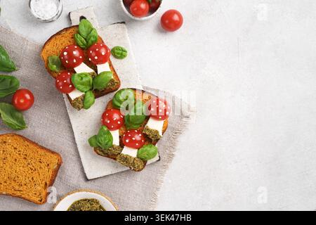 Flache Aussicht von oben auf zwei kreative offene Sandwiches, die in Form von Amanita-Pilzen mit Kirschtomaten und Mozzarella gestaltet sind, serviert auf weißer Keramik Stockfoto