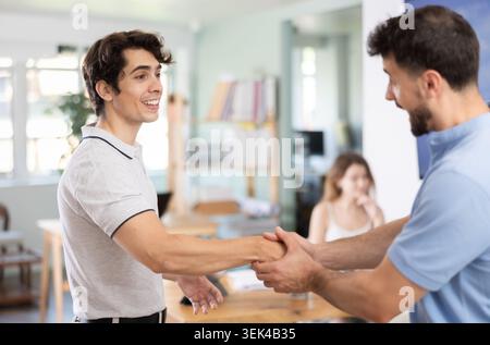 Ein junger Mann schüttelt dem Kollegen im Amt die Hand Stockfoto
