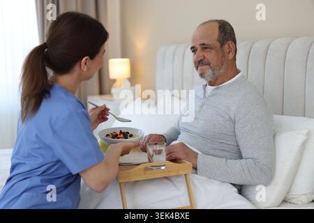 Die Pflegekraft frühstückt einem älteren Mann zu Hause im Bett Stockfoto