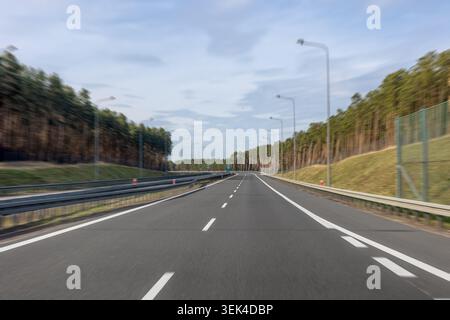 Leere Schnellstraße, die durch einen dichten Wald führt. Die Straße führt in die Distanz. Stockfoto