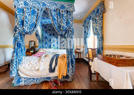 Carlyle House Daughters Room Blue Floral Canopy Bed Old Town Alexandria United States / ALEXANDRIA, Virginia — Ein blau-weißes, geblümtes Himmelbett dominiert das obere Schlafzimmer, das von den Töchtern des Kaufmanns John Carlyle genutzt wurde. Die umfangreichen passenden bedruckten Textilien spiegeln den hohen Wert des Stoffes in der Kolonialwirtschaft des 18. Jahrhunderts wider. Carlyle nutzte sein transatlantisches Schifffahrtsnetz, um diese teuren Materialien zu importieren, was seiner Familie sowohl Winterschutz als auch eine auffällige Darstellung des Reichtums verschaffte. Stockfoto