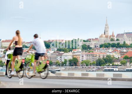 Unfokussiertes junges Paar, das Fahrrad entlang der Donau in Budapest fährt, vor dem Blick auf die Altstadt Stockfoto