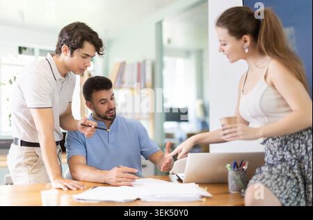 Positive junge Kollegen, die über Papiere auf dem Bürotisch diskutieren Stockfoto