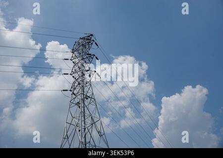 Ein niedriger Winkel eines Stahlgitterturms mit Hochspannungsleitungen unter einem hellblauen Himmel mit flauschigen weißen Wolken. Stockfoto