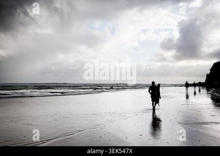 Surfer, die bei Sonnenaufgang an der Gold Coast, Queensland, Australien, entlang der Küste spazieren. Stockfoto