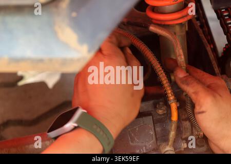 Fleißige mechanische Handreparatur der Aufhängung am Fahrzeug mit schmutzigen Fingern, die während der Wartungsarbeiten einen Smartwatch-Haltedraht tragen, wobei konzentrierte Sorgfalt geboten ist Stockfoto