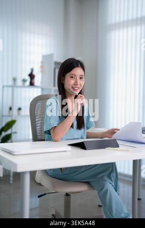 Asiatische junge Erwachsene weibliche Ärztin in Peelings Uniform Überprüfung Dokumente an hellen modernen Bürotisch Stockfoto