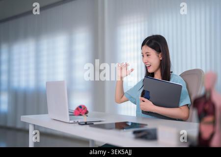 asiatische Frau professionelle winkende Hand Gruß während Online-Videokonferenz Anruf halten Ordner Laptop modernes Büro Stockfoto