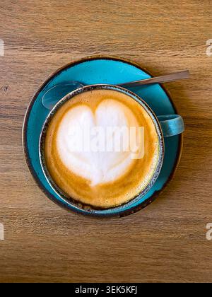 Herzförmige Latte Art in blauer Tasse mit Löffel Stockfoto