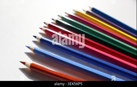 Ein Satz farbiger Bleistifte ist ordentlich auf einer weißen Oberfläche angeordnet. Das Sonnenlicht hebt die leuchtenden Farben jedes Bleistifts hervor. Diese Szene zeigt Werkzeuge zum Zeichnen oder Färben. Stockfoto