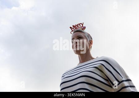 Frau mittleren Alters, die draußen steht, trägt einen gestreiften Pullover, ein rotes Weihnachtsband, einen Anhänger, einen Kopierraum Stockfoto