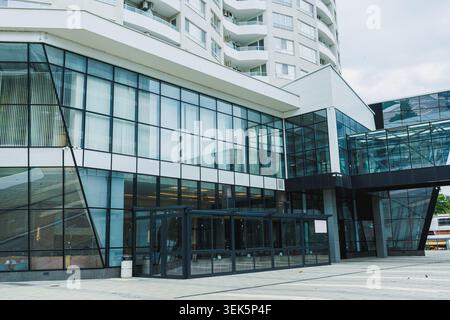 Ein großes Gebäude mit Glasfassade und modernem Design. Es steht tagsüber in einem Stadtgebiet mit klarem Himmel. Man kann Leute beim Gehen sehen Stockfoto