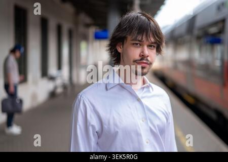 Junger Mann in weißem Hemd, der im Sommer auf einem Bahnsteig in der Nähe des Zuges steht Stockfoto