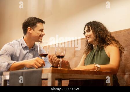 Junge Paare verbringen einen entspannten Moment zusammen, während sie Gläser Rotwein in einem gemütlichen Restaurant genießen. Romantisches kulinarisches Erlebnis, geselliges miteinander Stockfoto