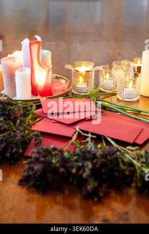 Verstreute rote Umschläge zwischen getrockneten Lavendelzweigen und Kristallvotiven mit schmelzenden Kerzen auf Messingtablett auf dunklem Holzboden. Kräuterzeremonie setti Stockfoto