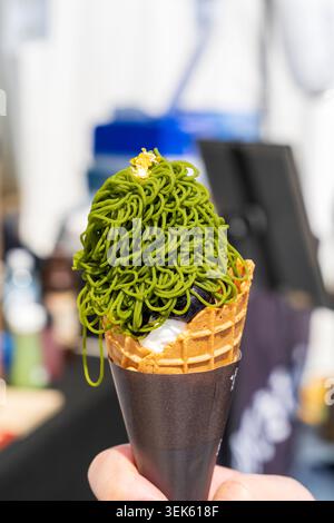 Eiskegel mit Matcha-Tee-Geschmack. Handhaltung gewickelter Kegel mit Eiscreme, belegt mit Eisständern mit grünem Matcha-Tee-Geschmack. Stockfoto