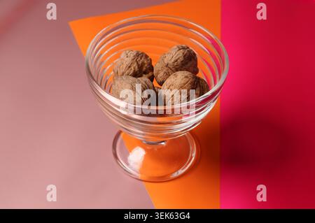 Vier ganze Walnüsse in einer Dessertschüssel aus klarem Glas auf farbenfrohem Hintergrund Stockfoto