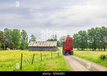 Traktor mit Wagen auf einer Feldstraße bei einer alten Scheune auf dem Land Stockfoto