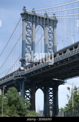 Flacher Blick auf eine große Hängebrücke aus Stahl mit Turm und Kabeln über einer Stadtstraße, eingerahmt von Bäumen und Himmel an einem klaren Tag. Stockfoto