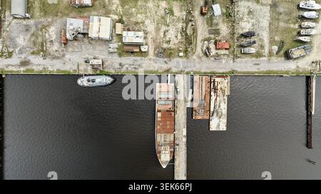 Aus der Vogelperspektive auf die industrielle Werft mit rostigen Lastkähnen, Booten am Pier und Lagercontainern entlang der Uferpromenade in Green Cove Springs, Flo Stockfoto