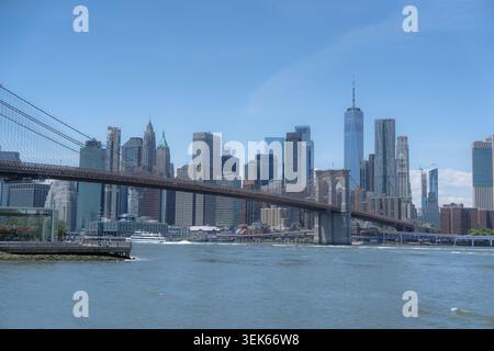Die Brooklyn Bridge überspannt den Fluss mit der Skyline von manhattan unter einem klaren blauen Himmel. Stockfoto