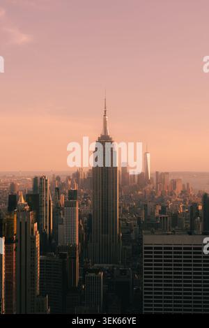 Skyline von New york bei Sonnenuntergang mit dem Empire State Building im Zentrum und warmrosa Himmel über hohen Wolkenkratzern. Stockfoto