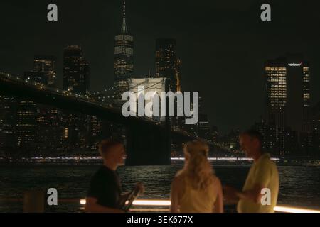 Nächtliche Skyline der Stadt mit brooklyn Bridge und unscharfen Menschen auf einer Terrasse am Wasser mit Blick auf die Skyline von manhattan. Stockfoto