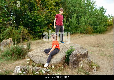 Bruder steht, während die jüngere Schwester auf Felsen sitzt Stockfoto