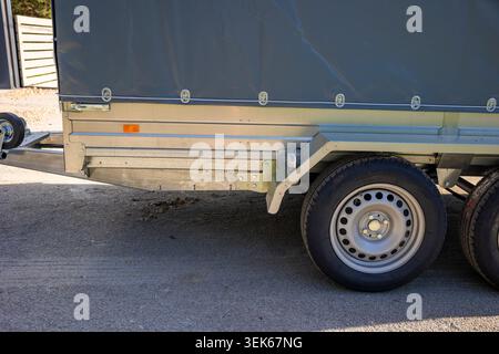 Nahaufnahme eines silbernen zweiachsigen Nutzanhängers mit Rädern auf einer sonnigen Einfahrt. Konzept: Transportlogistik Stockfoto