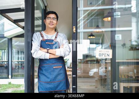 Eigentümer eines kleinen Unternehmens, der am Eingang des Ladens steht und das Schild „Open“ (offen) hat Stockfoto