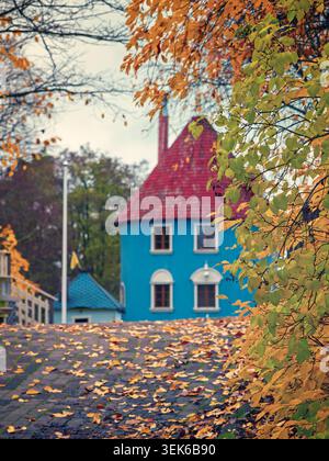 Naantali, Finnland - 31.10.2020: Malerischer Blick auf ein blaues nordisches Cottage unter goldenem Herbstlaub mit gefallenen Blättern auf Kopfsteinpflaster Stockfoto