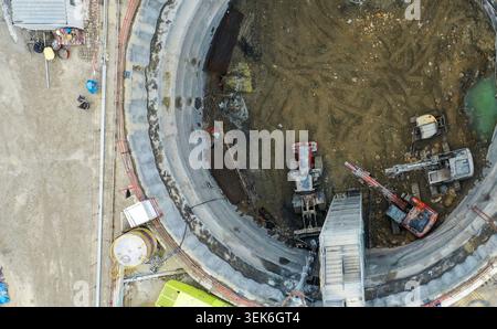 Luftaufnahme von schweren Maschinen, einschließlich Baggern und Ladern, die in einem großen kreisförmigen Ausschachtschacht auf einer Industriebau in arbeiten Stockfoto