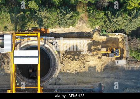Aus der Vogelperspektive einer Baustelle mit einem großen kreisförmigen Schacht, einem gelben Portalkran und einem Bagger, der Boden in der Nähe eines Waldes in Avcilar gräbt, ist zu sehen Stockfoto