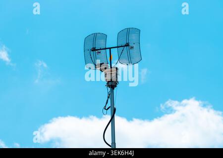 4K-Aufnahme einer professionellen Rundfunkantenne mit zwei großen Reflektoren mit Parabolraster, die auf einem Metallmast vor einem leuchtend blauen Himmel montiert sind, SEL Stockfoto
