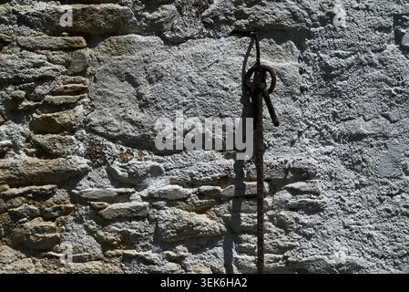 Altes Pferdegeschirr aus Metall hängt an einer weiß getünchten Steinmauer Stockfoto