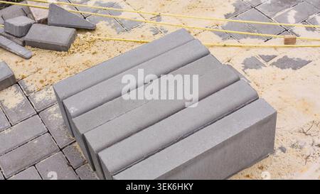 Eine Reihe grauer Betonsteine steht auf einer sandigen Baustelle während eines Pflastervorgangs Stockfoto