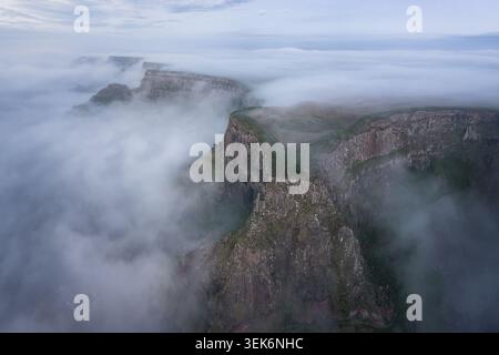 Blick aus der Vogelperspektive auf die Klippen des Giant's Causeway, umgeben von dickem Morgennebel und Nebel mit grünen Plateaus und Basaltfelsen in Bushmills, Norther Stockfoto